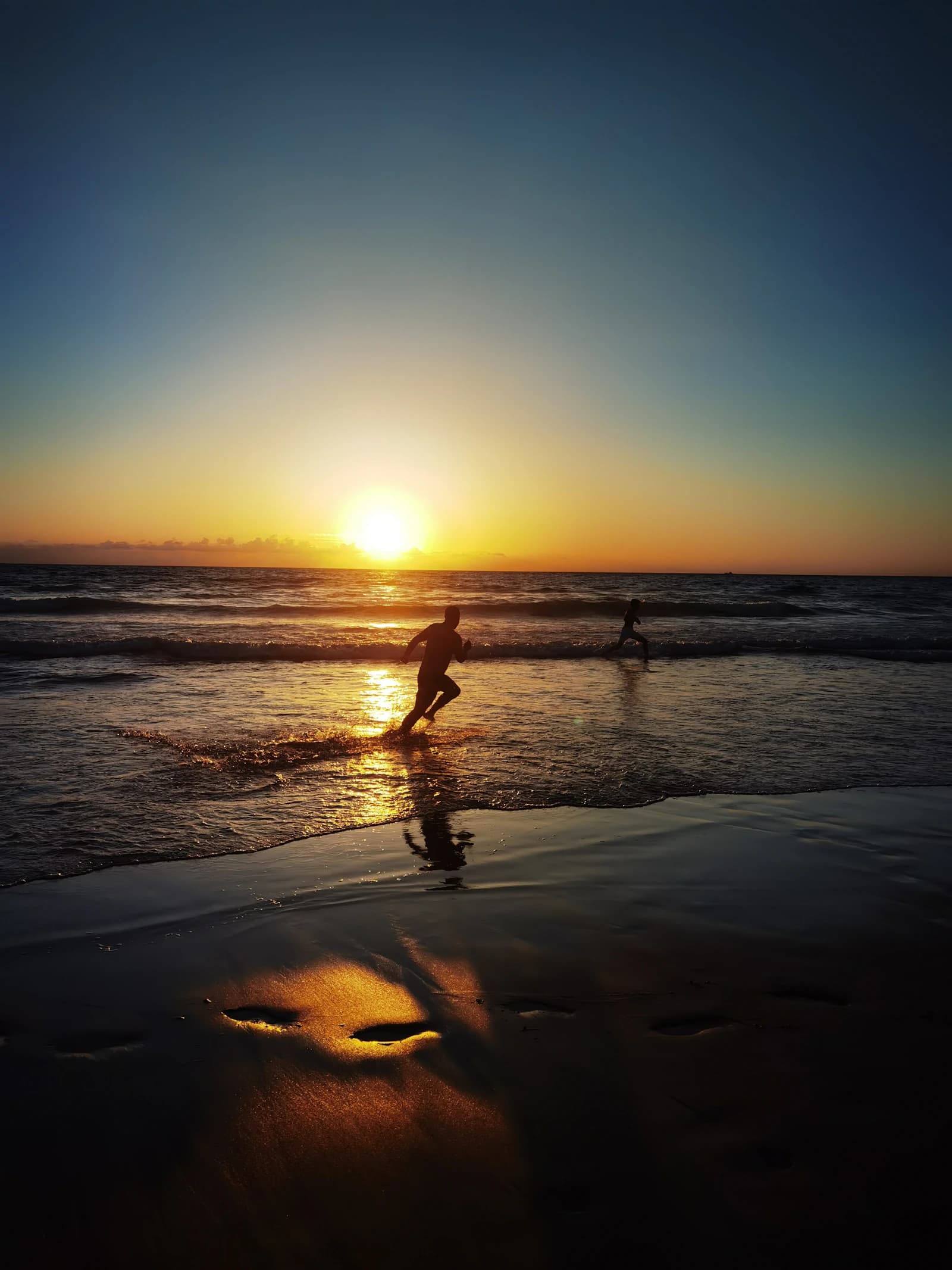 Two people running through the sea at sunset, with golden light reflected in the sand