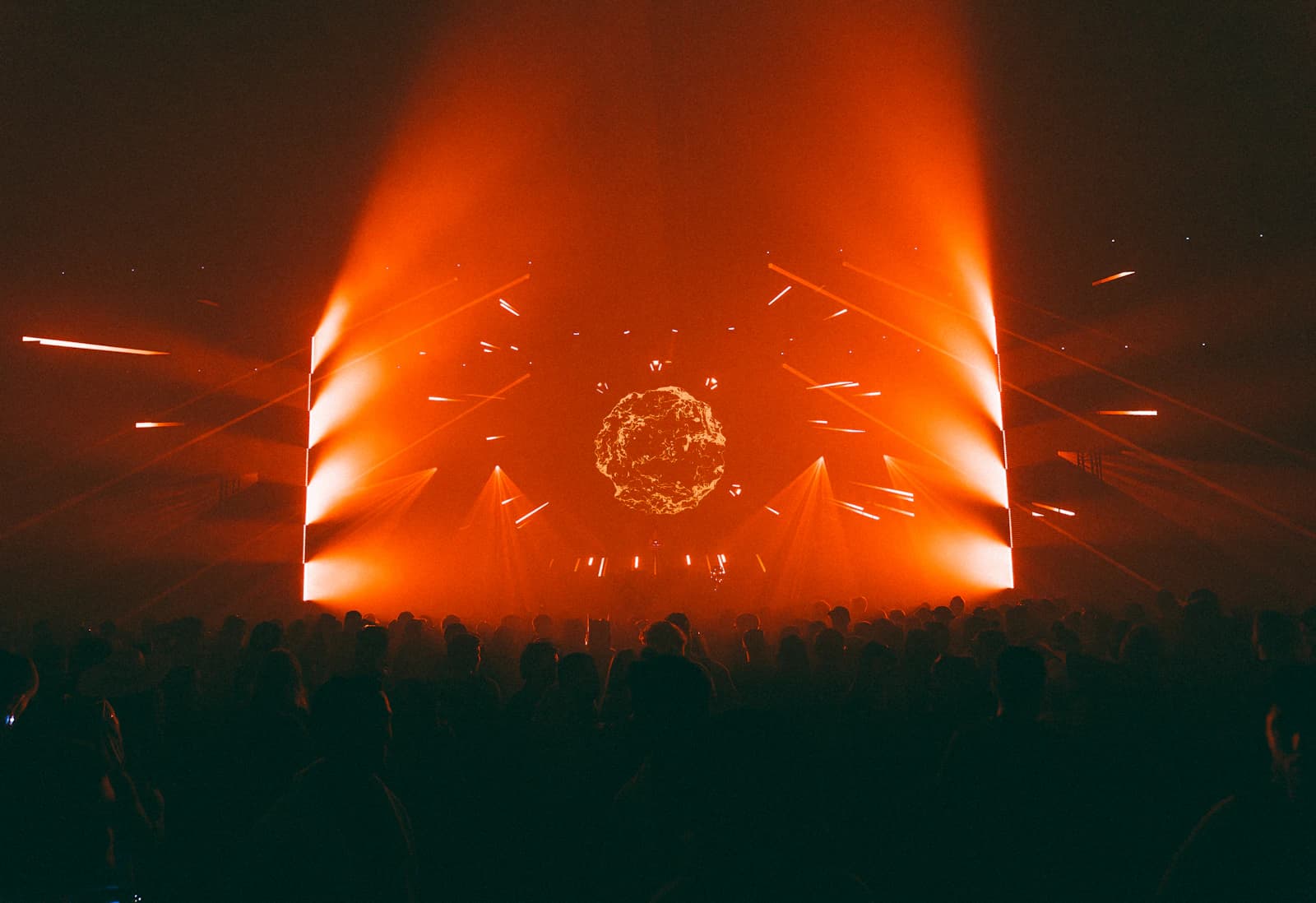 A festival crowd facing a monumental stage lit by symmetrical amber beams