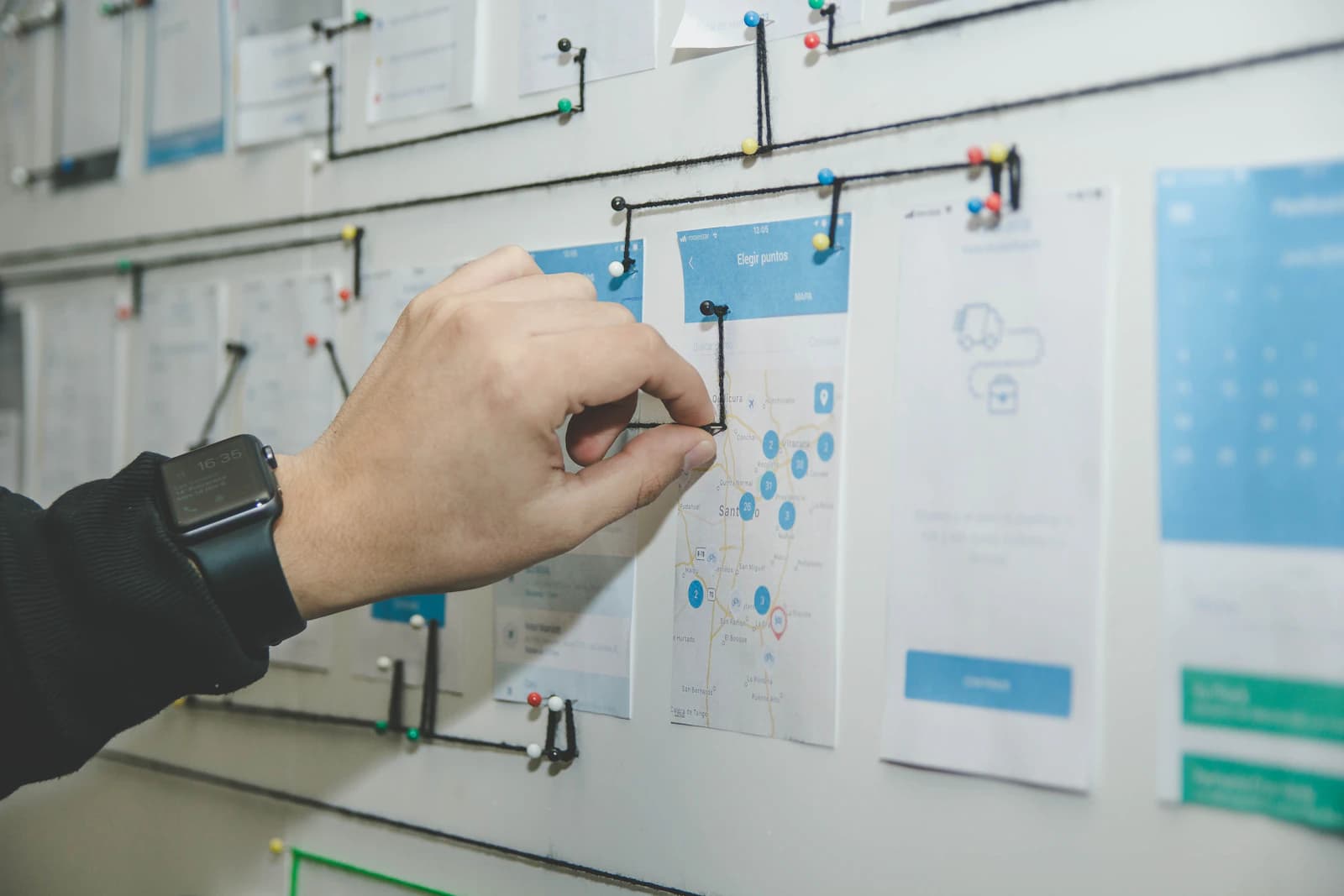A hand connecting paper interface sketches to map a product journey
