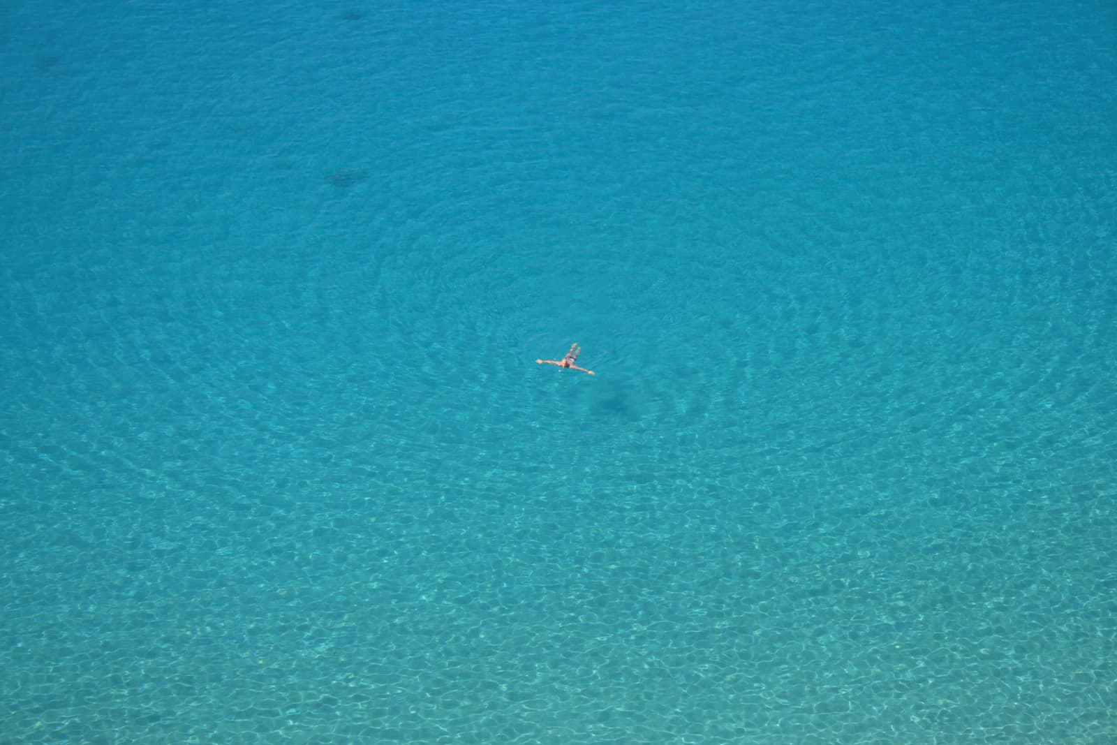 A lone swimmer floating in clear turquoise water, seen from above